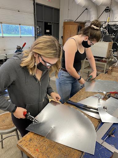 SMDCVI grade 12 students Jenna Switzer and Adrianne Butler using tin snips to hand cut sheet metal pieces for their ductwork