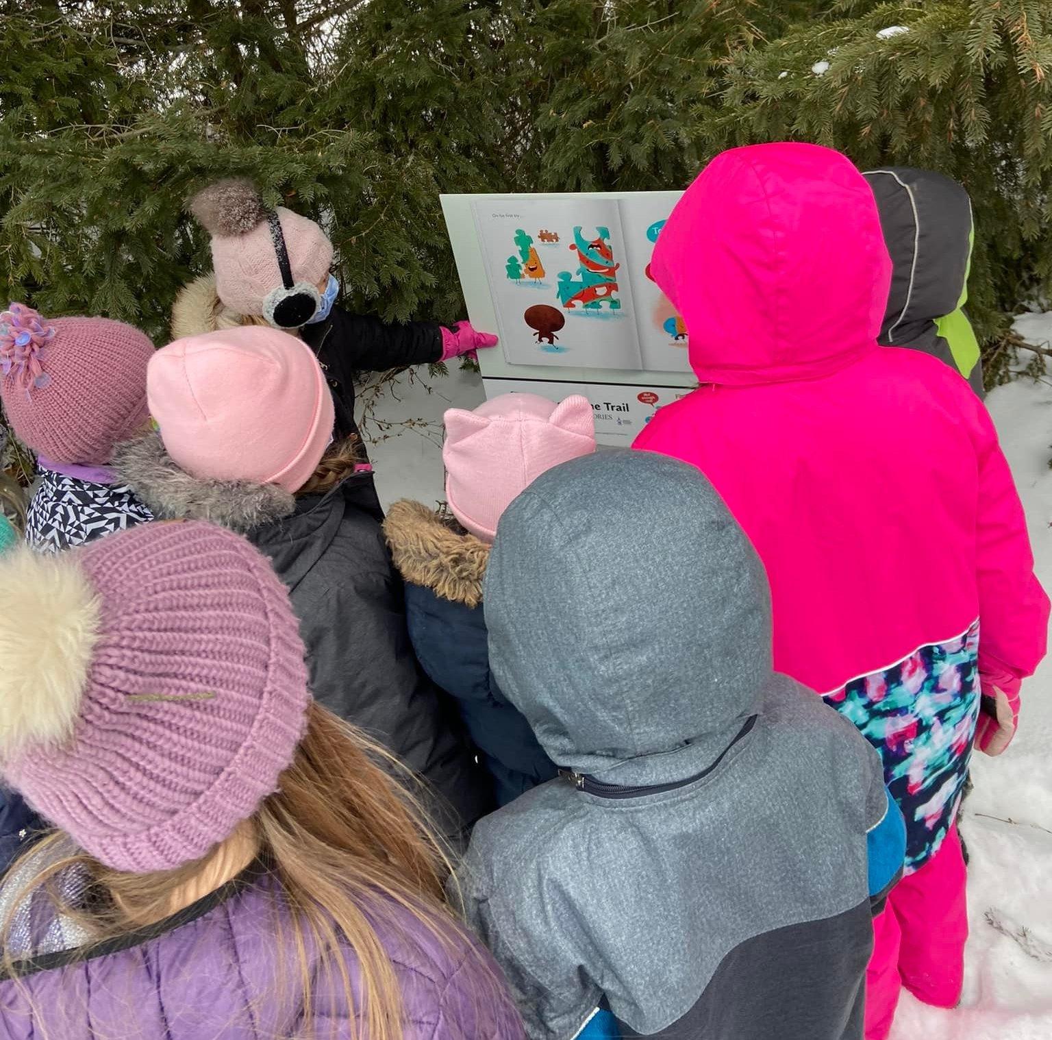Image showing students wearing winter gear looking at sign containing part of a story outdoors