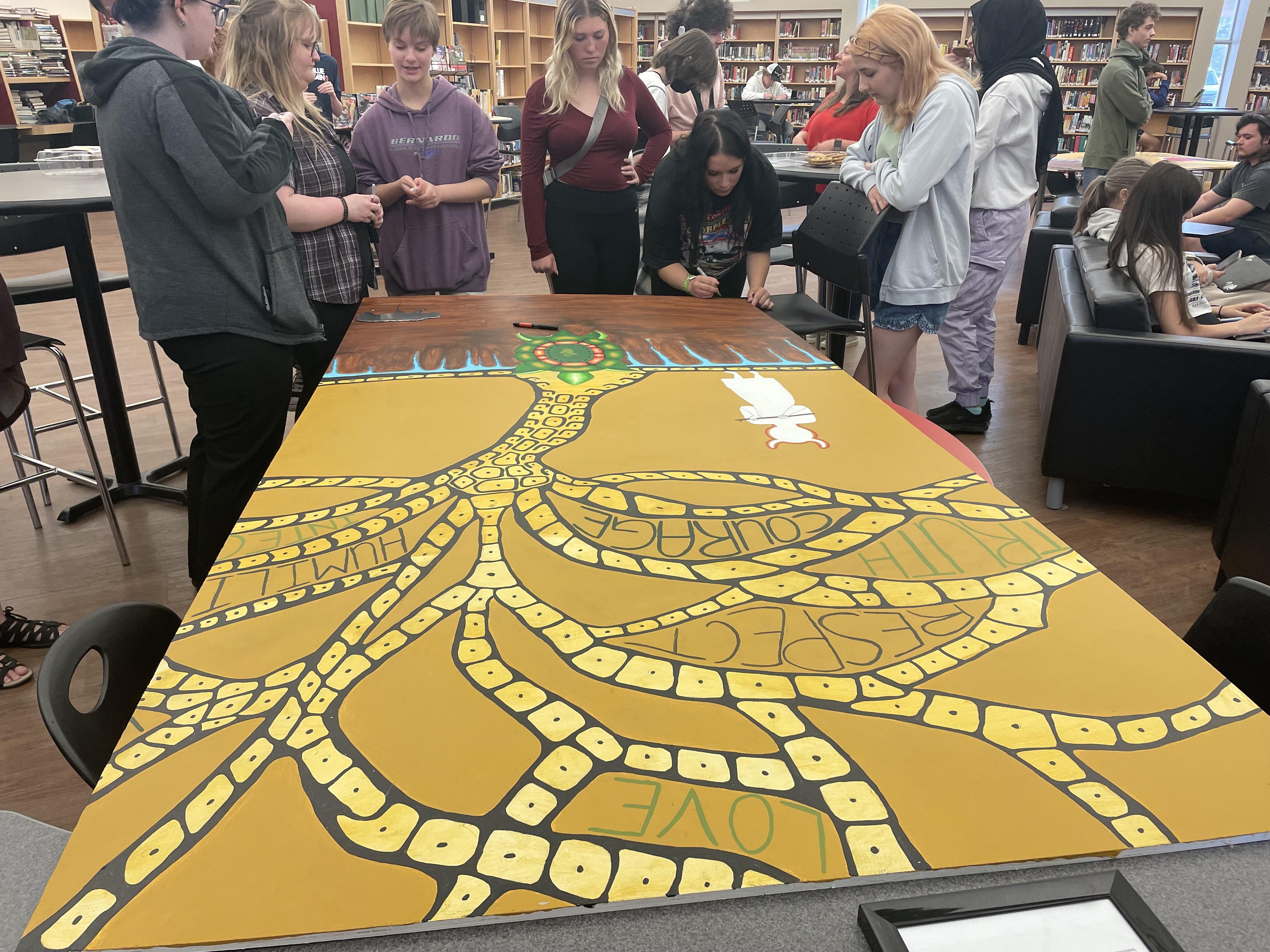 Image of students signing the art piece while it rests on a table